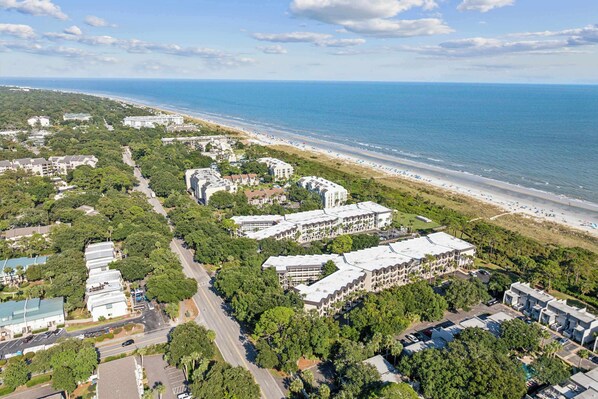 An aerial view of a coastal hotel area with multiple buildings, a beach, and a road.