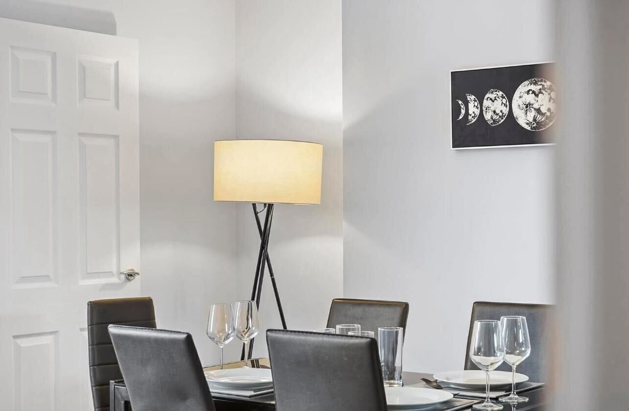 A dining area with a table set for two, a floor lamp, and a wall-mounted artwork depicting the moon phases.