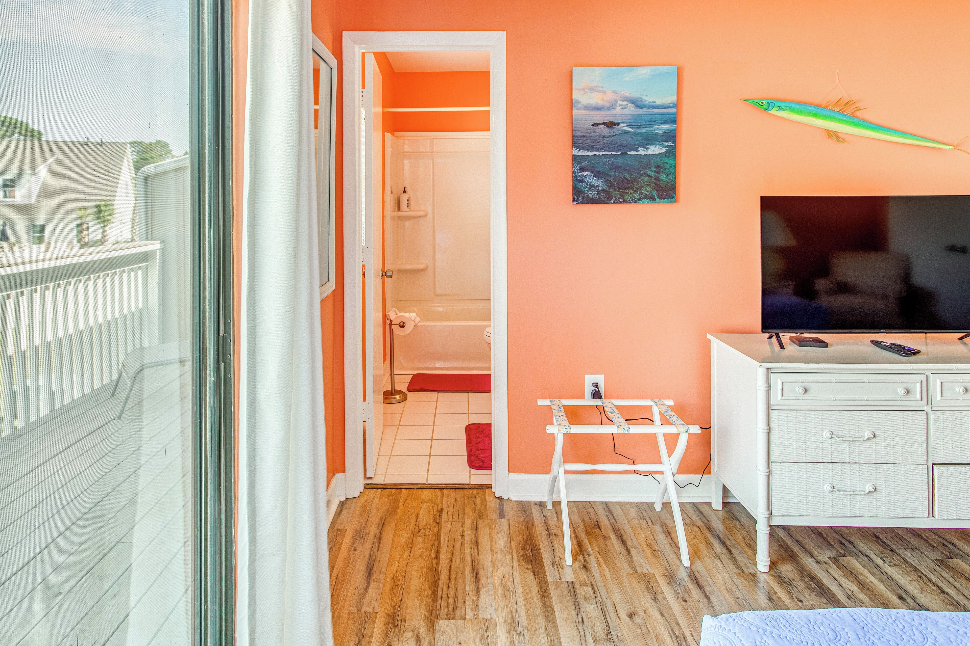 A room with a wooden floor, a white dresser, a television, and a painting of a fish on the wall.