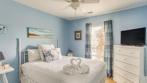 Un dormitorio con cama, cómoda, televisor y ventilador de techo.