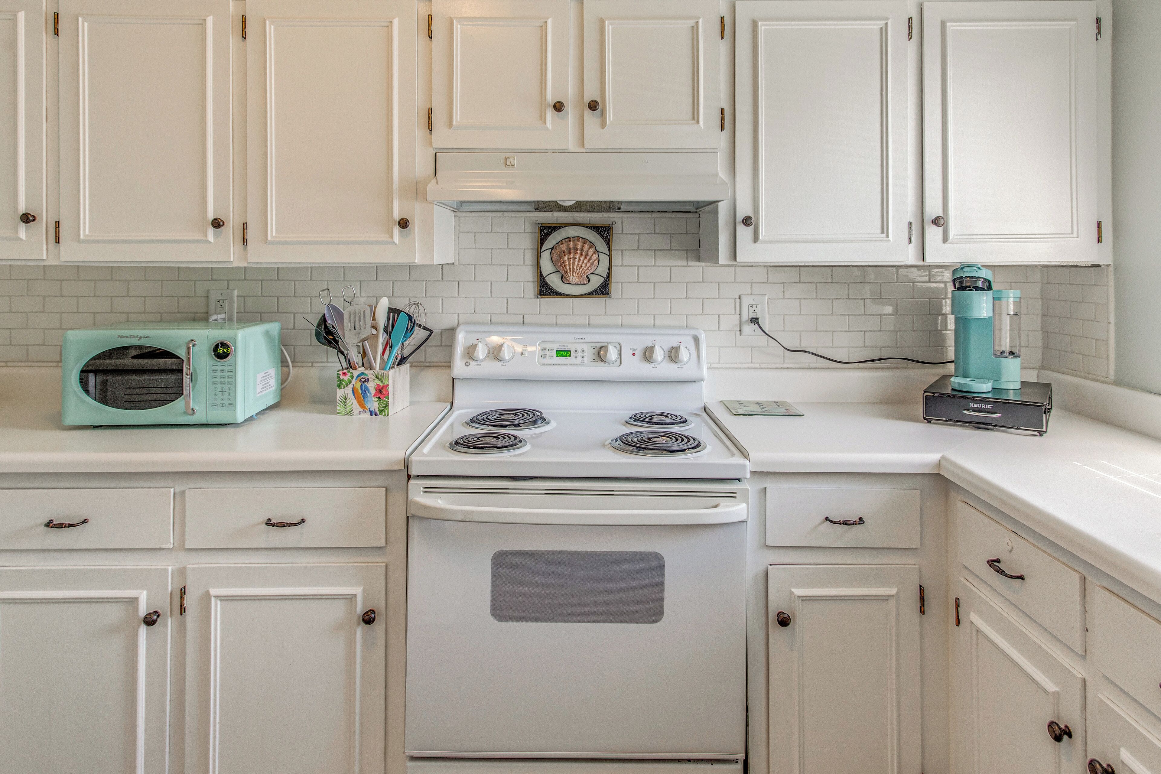 A kitchen with white cabinets, a white stove, a teal microwave, and a teal coffee maker.