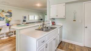 Una cocina moderna con armarios blancos, un lavamanos doble y una zona de comedor con mesa y sillas.