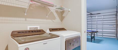 A laundry area with two Whirlpool dryers, a metal shelf with laundry baskets, and a view of a garage with a blue floor.