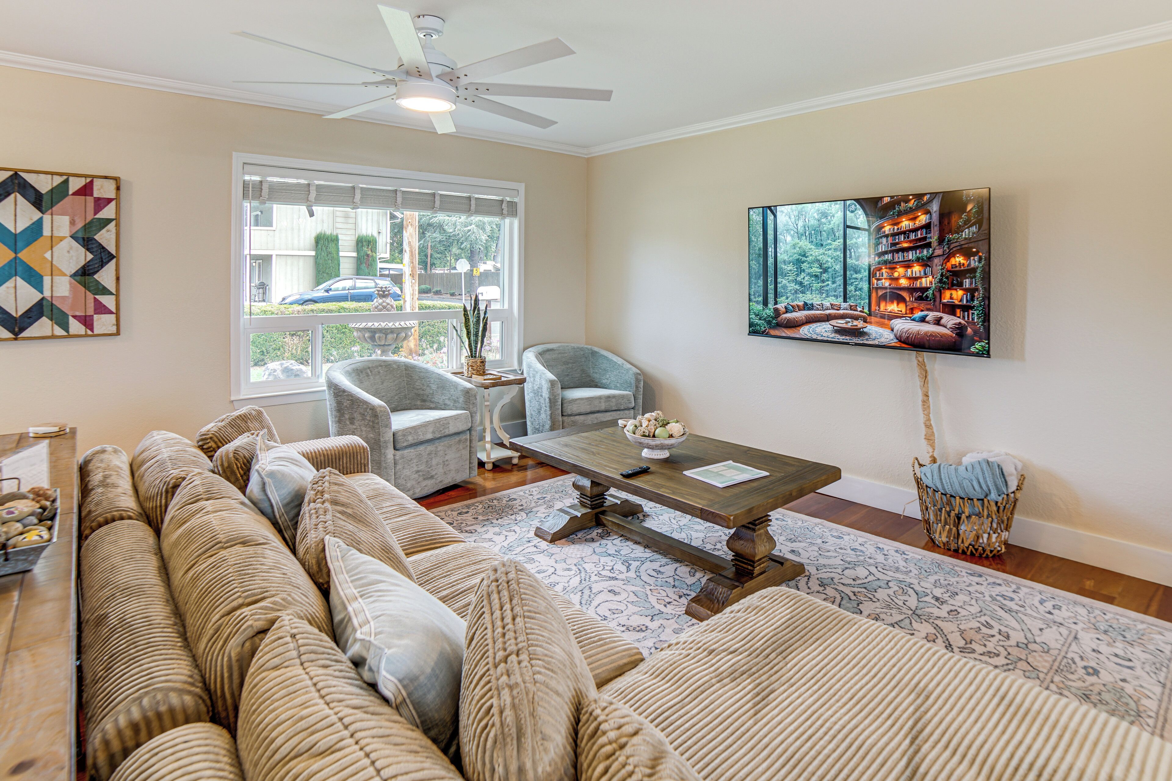 A living room with a large sofa, armchairs, a coffee table, and a television on the wall.