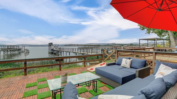 A deck with outdoor furniture, a glass table, and a red umbrella.