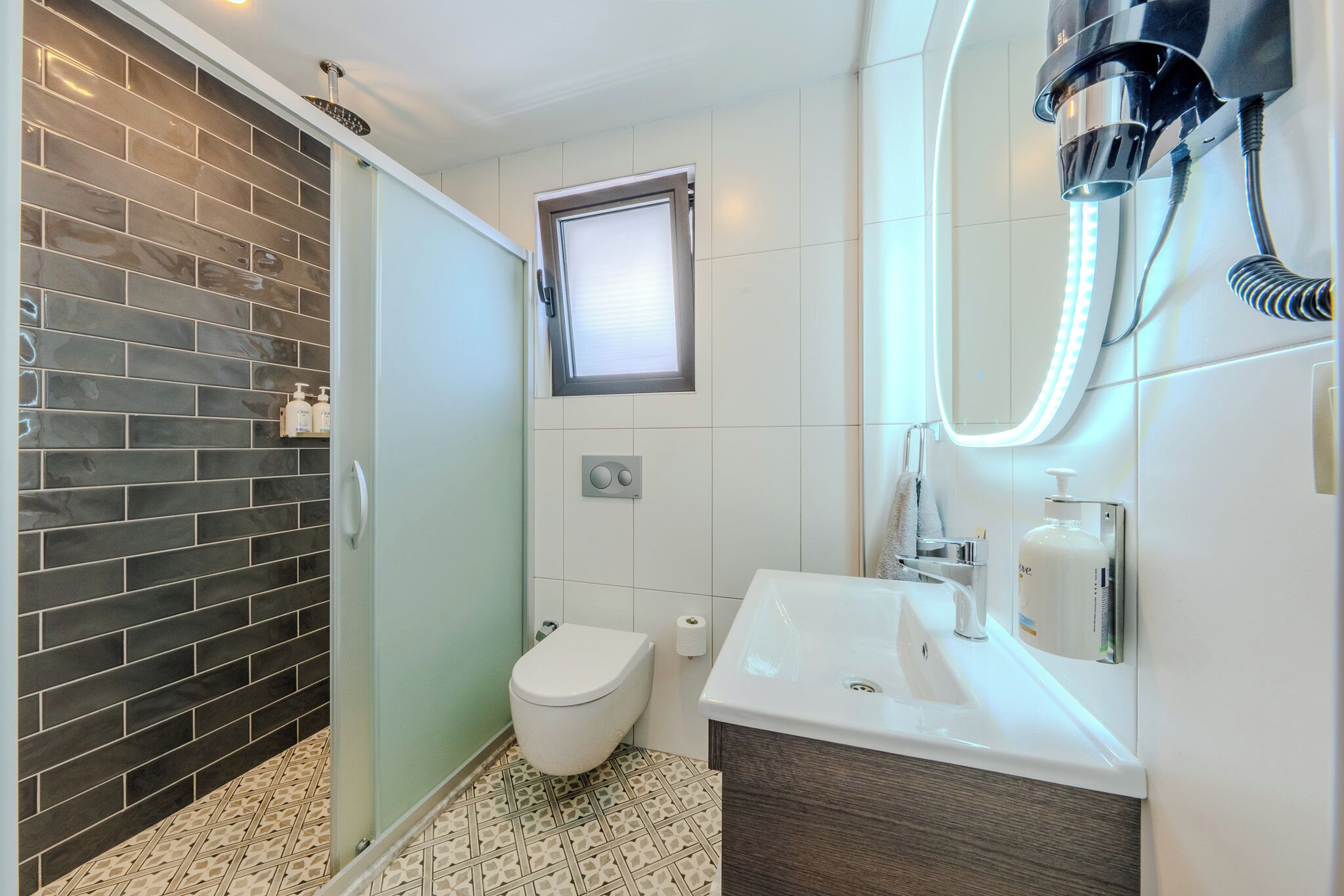 A modern bathroom with a glass shower enclosure, a toilet, a sink with a mirror, and a window.