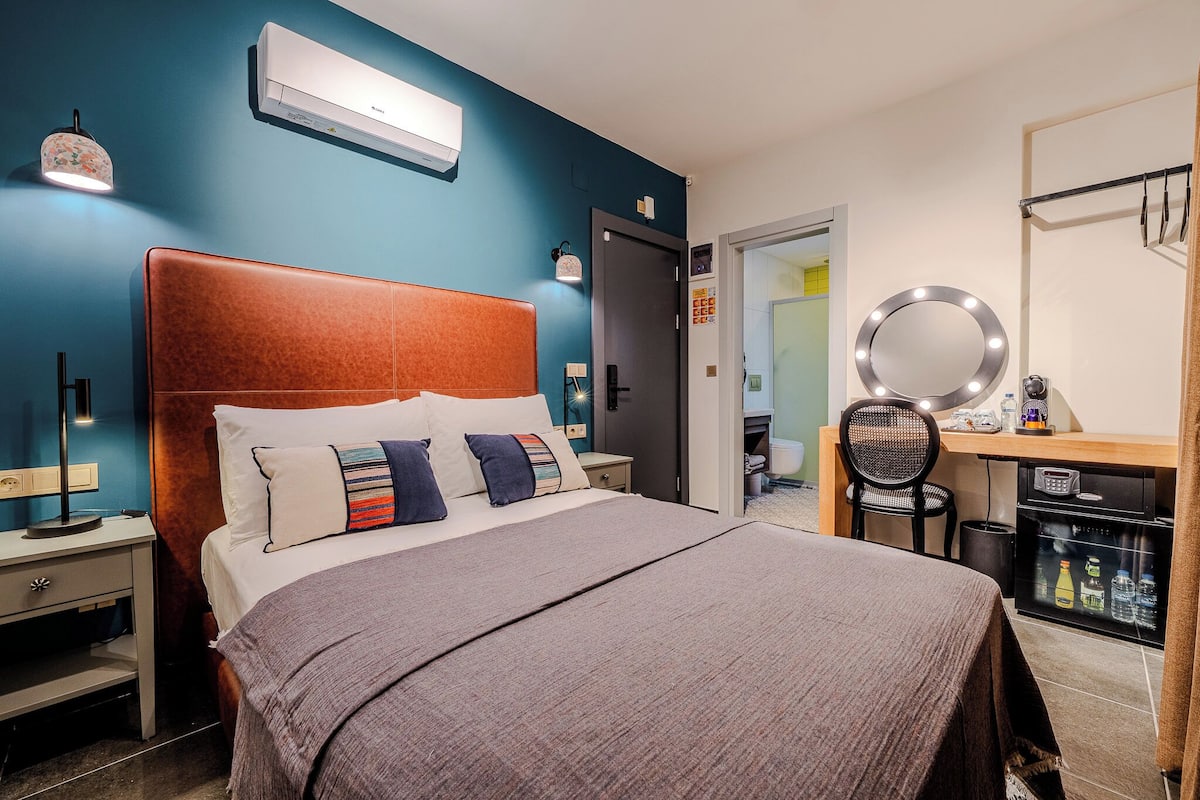 Een moderne hotelkamer met een groot bed, een bureau met spiegel en een minibar.