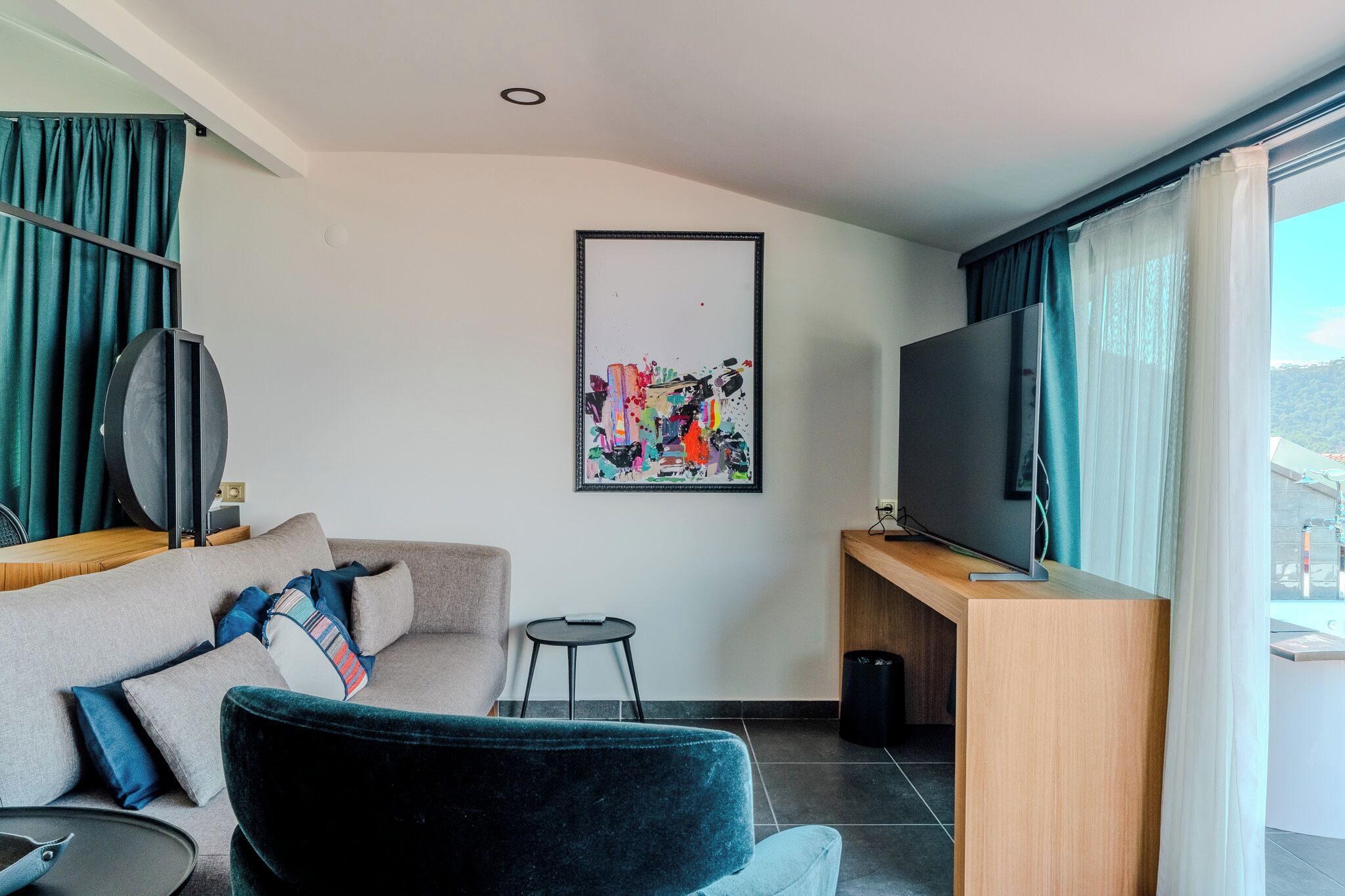 Uma sala de estar moderna com um sofá, uma poltrona preta, uma mesa pequena, uma televisão e um quadro na parede.