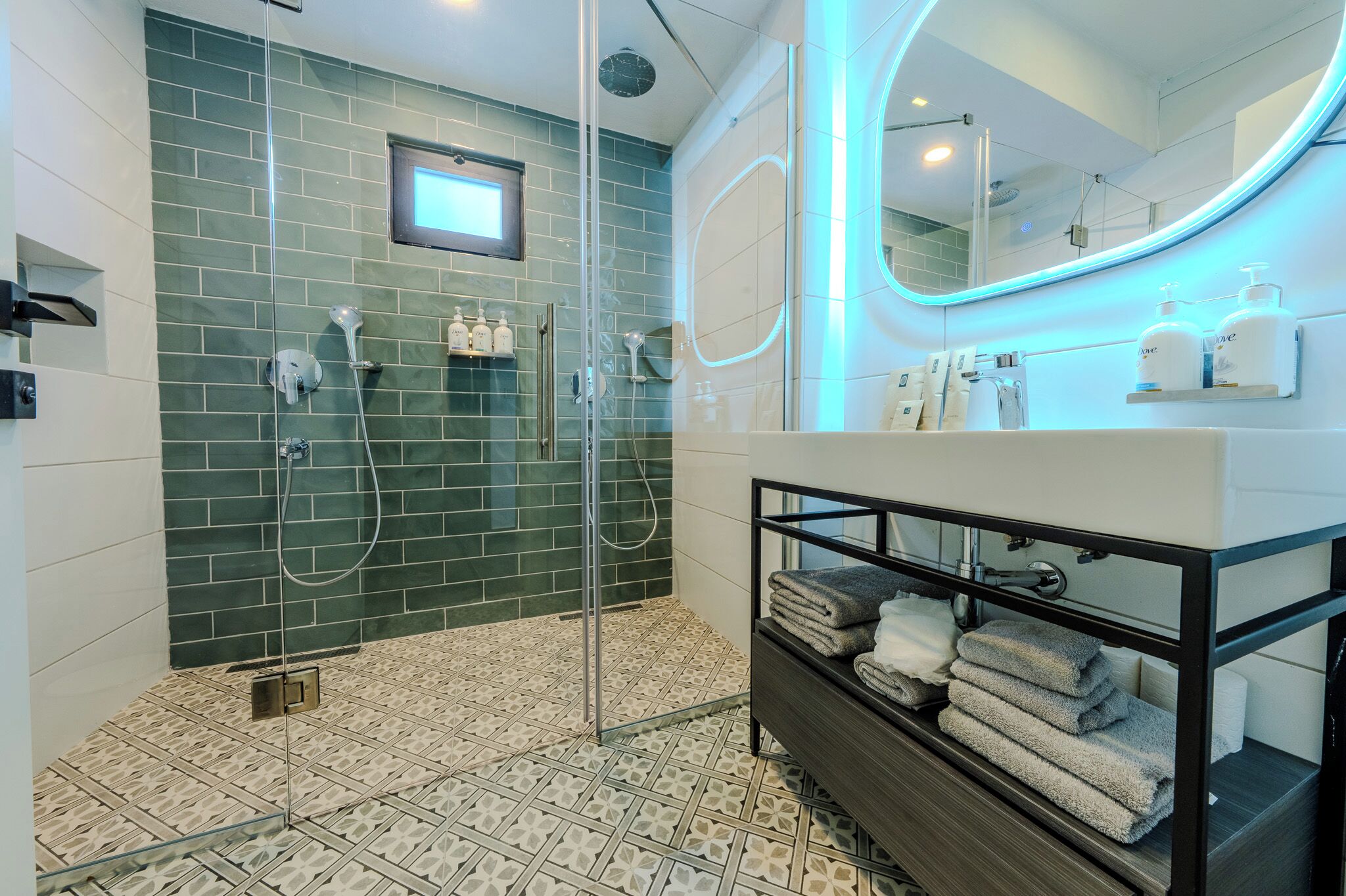 A modern bathroom with a glass-enclosed shower, a large mirror, and neatly stacked towels.