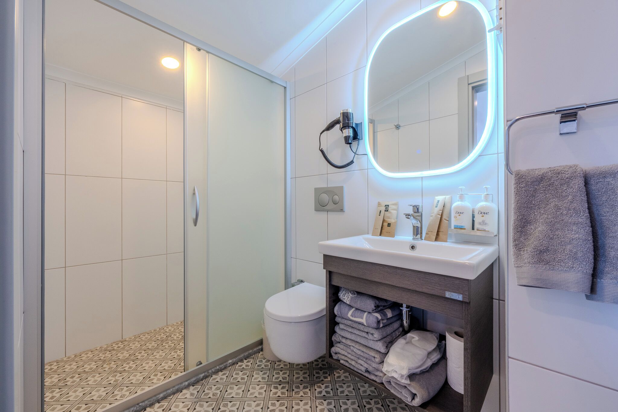 Een moderne badkamer met een douchecabine van glas, een wit toilet, een wastafel met spiegel en netjes gevouwen handdoeken.