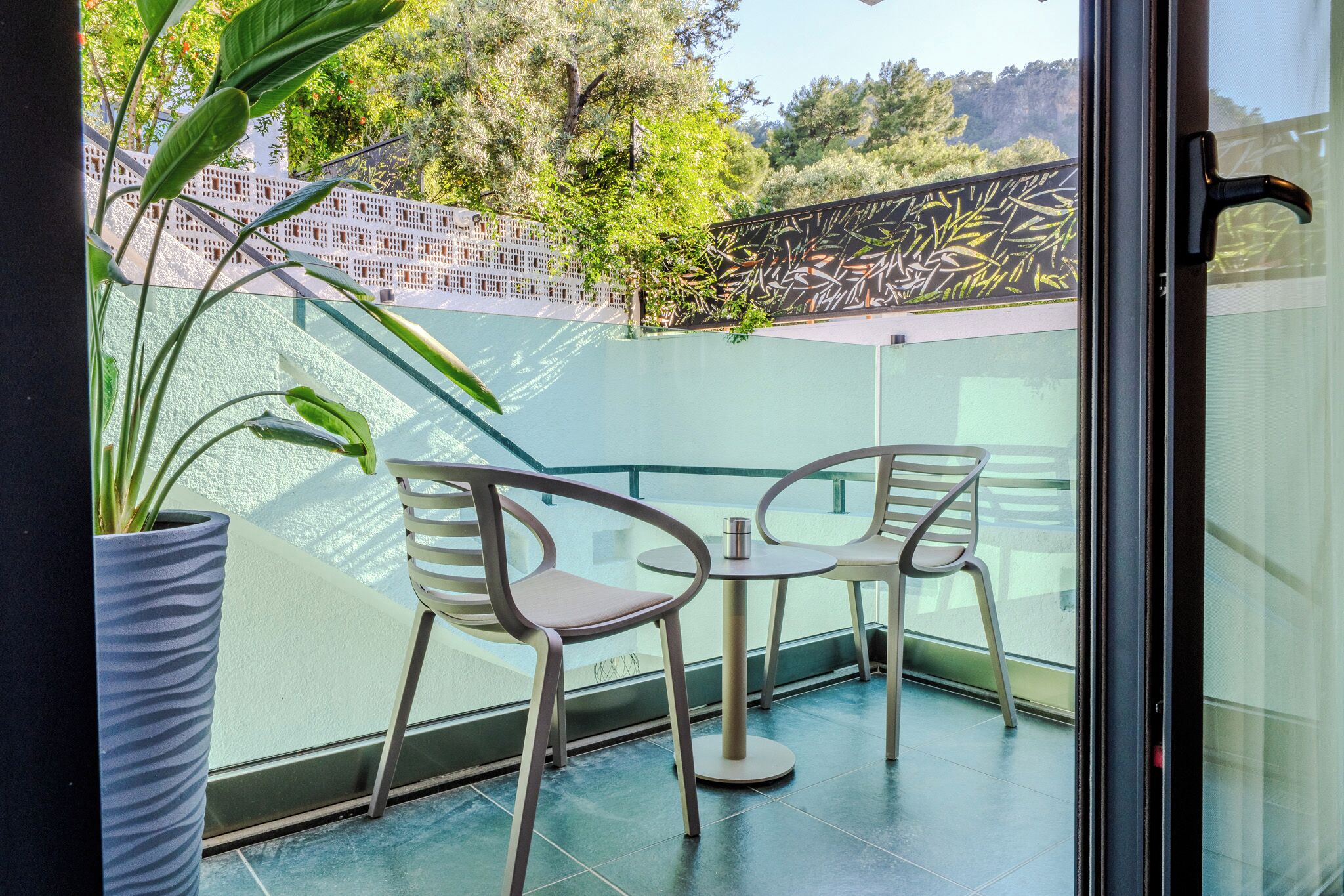 A balcony with two chairs and a table, a potted plant, and a decorative wall.