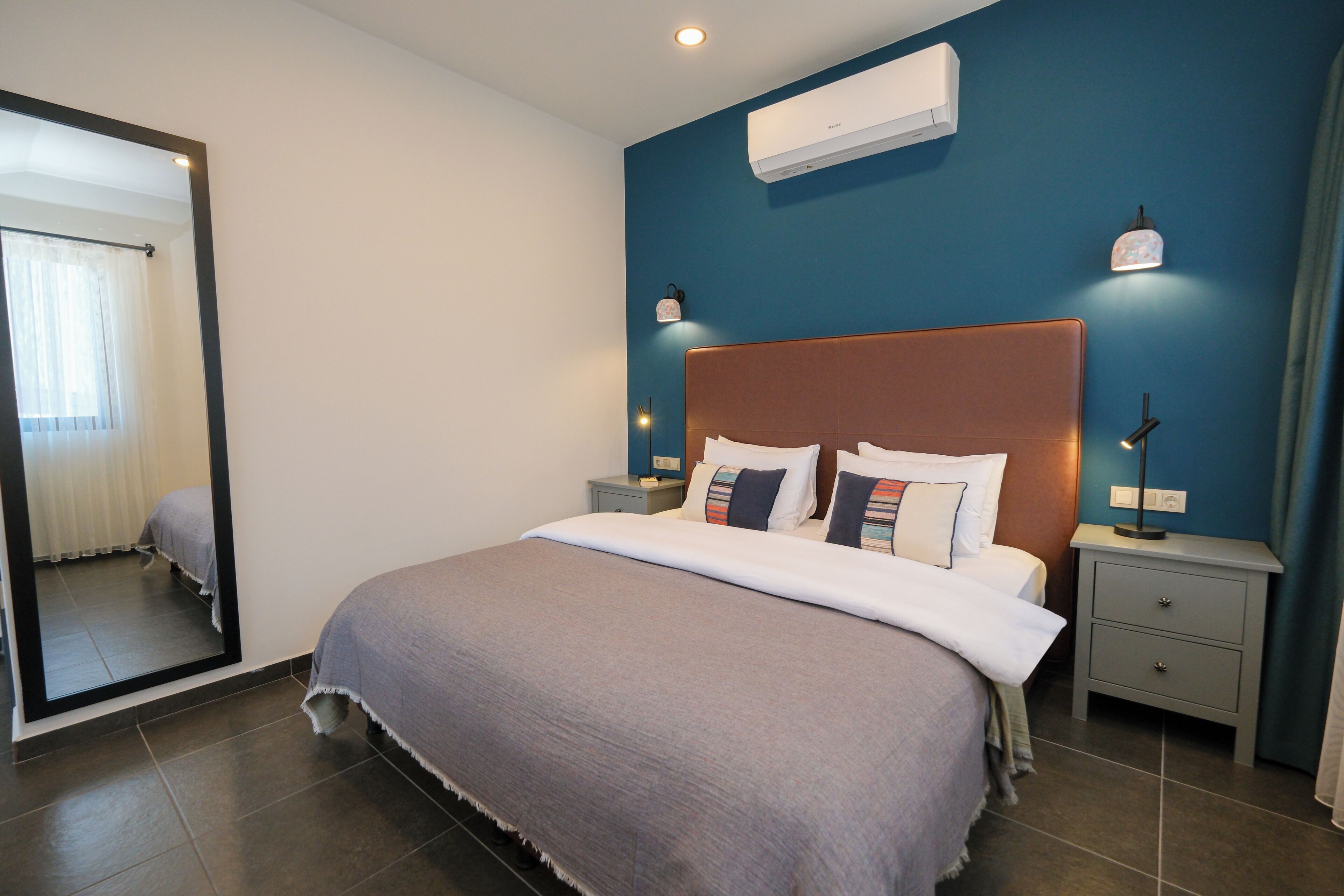 A bedroom with a bed, nightstands, a mirror, and an air conditioning unit.