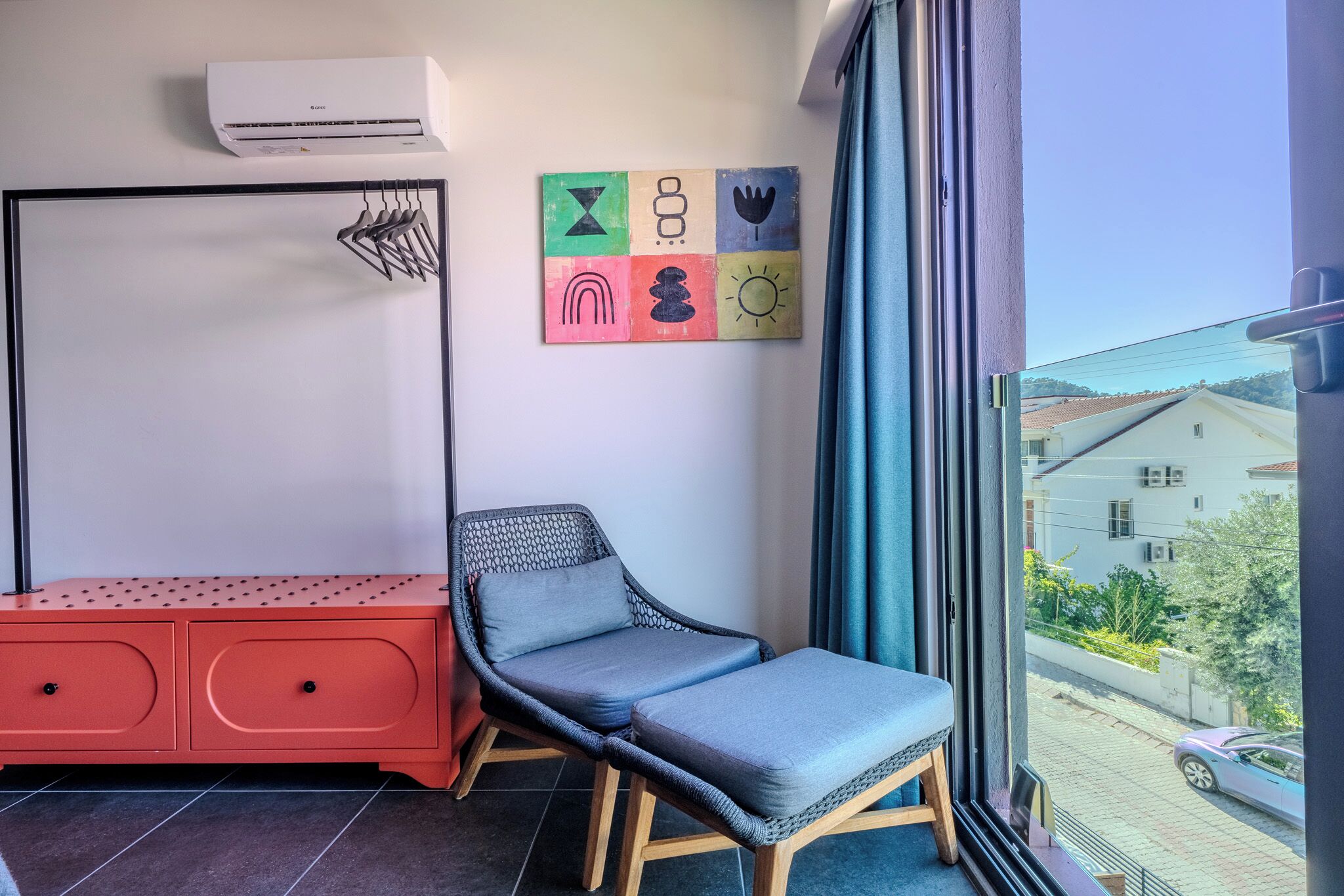 A balcony with a wicker chair, a red cabinet, and a wall-mounted air conditioner.