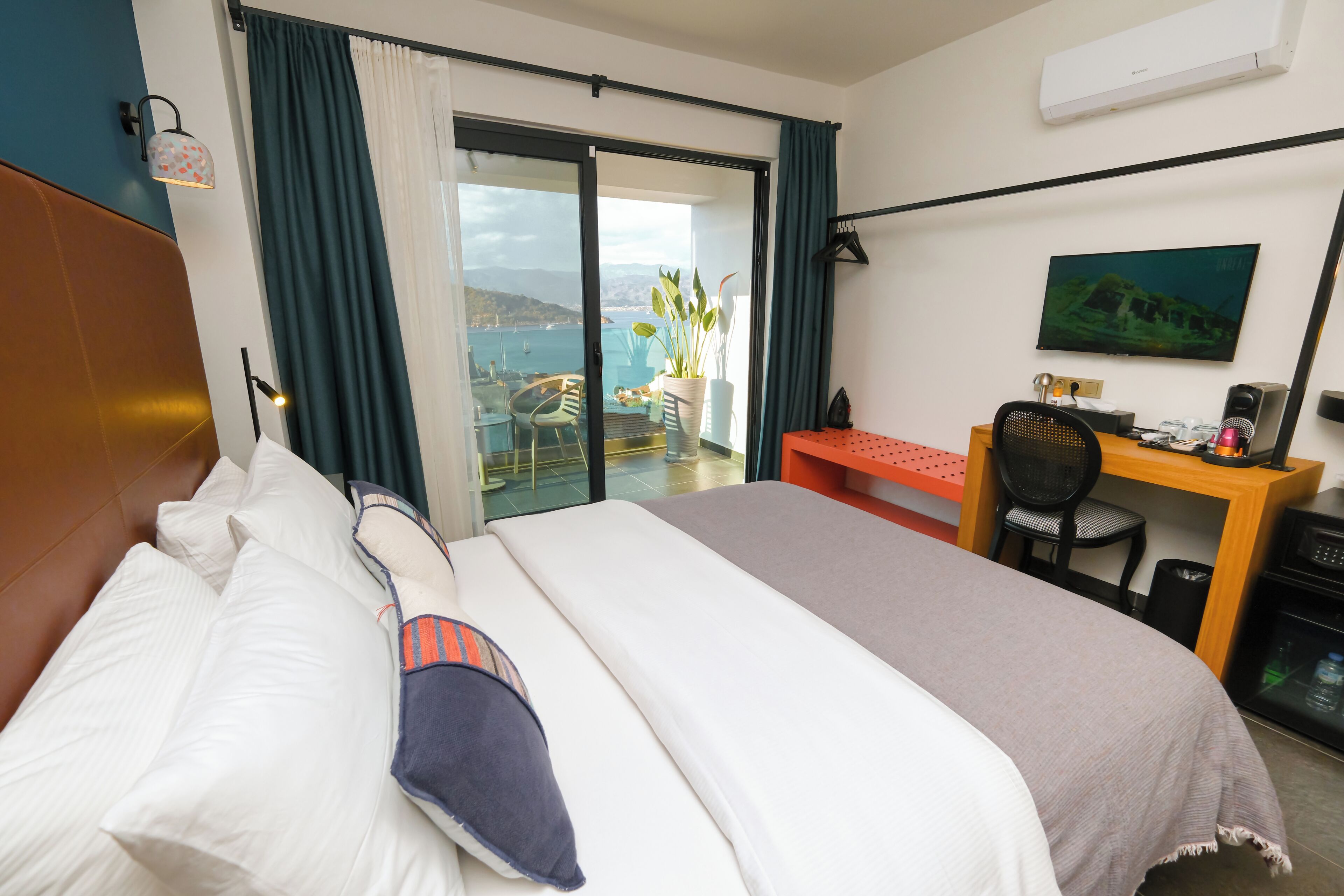 A hotel room with a bed, a desk, a chair, a TV, and a view of the sea.