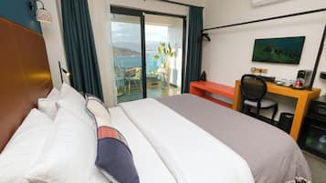 Habitació d'hotel amb llit, escriptori, cadira, televisió i vista al mar.