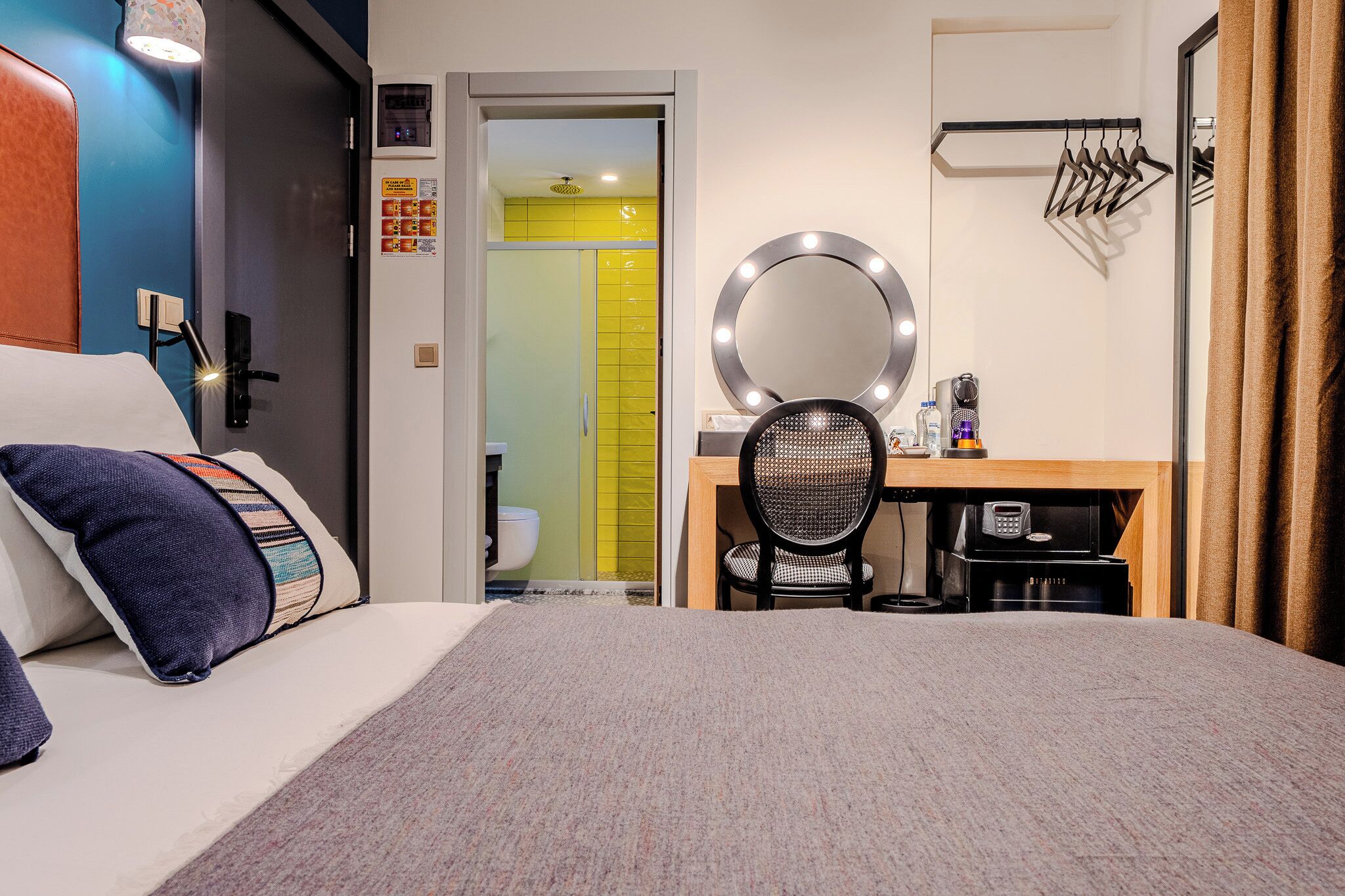 A hotel room with a bed, a desk with a chair, a mirror, and a bathroom visible through an open door.