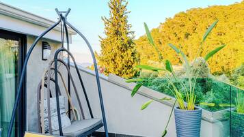 A modern outdoor seating area with a swing chair, a potted plant, and a view of a forested hillside.