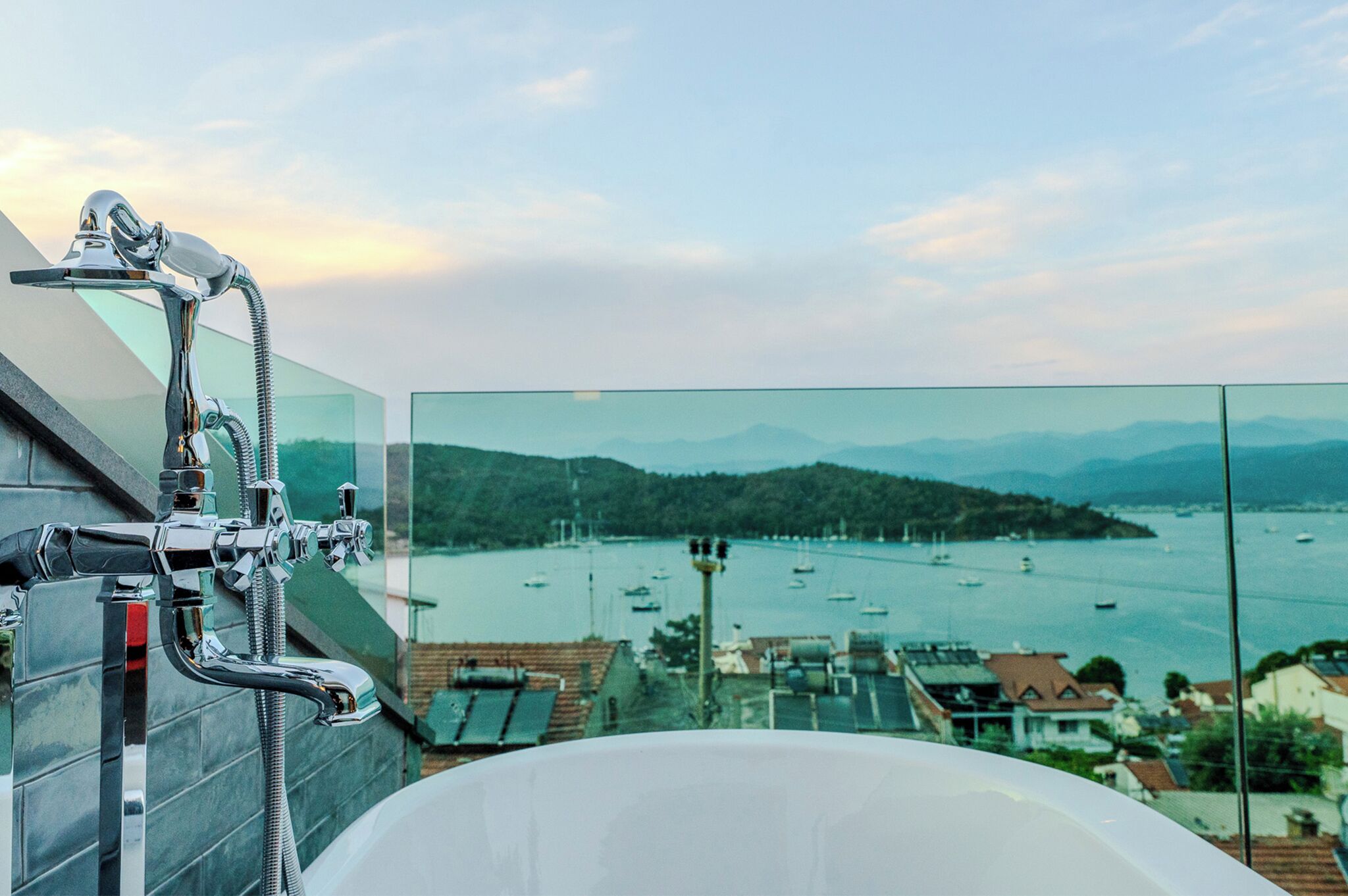 A bathroom with a bathtub and a shower with a view of a bay with boats.