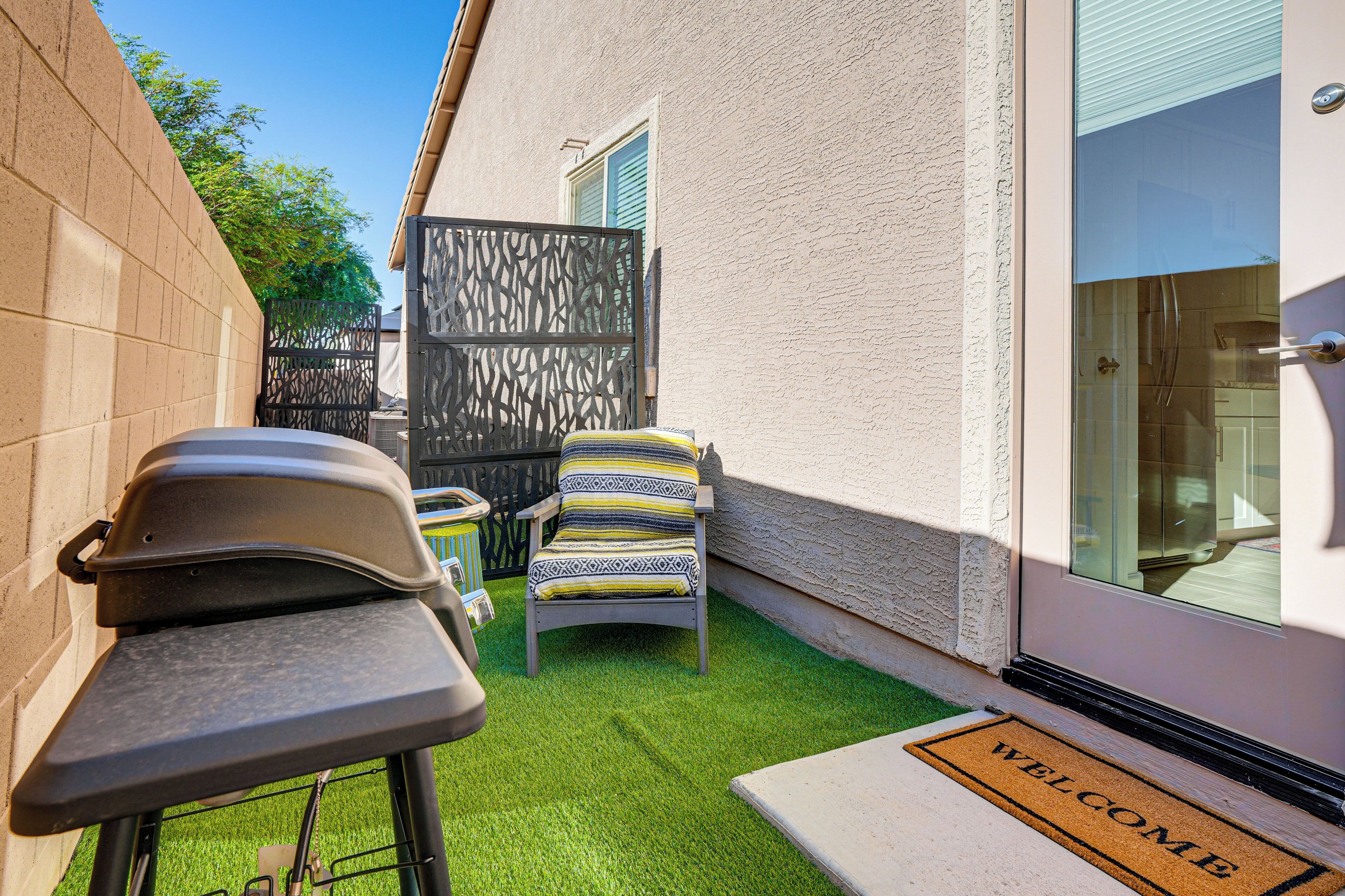 A small outdoor patio with a barbecue grill, a cushioned chair, and a welcome mat.
