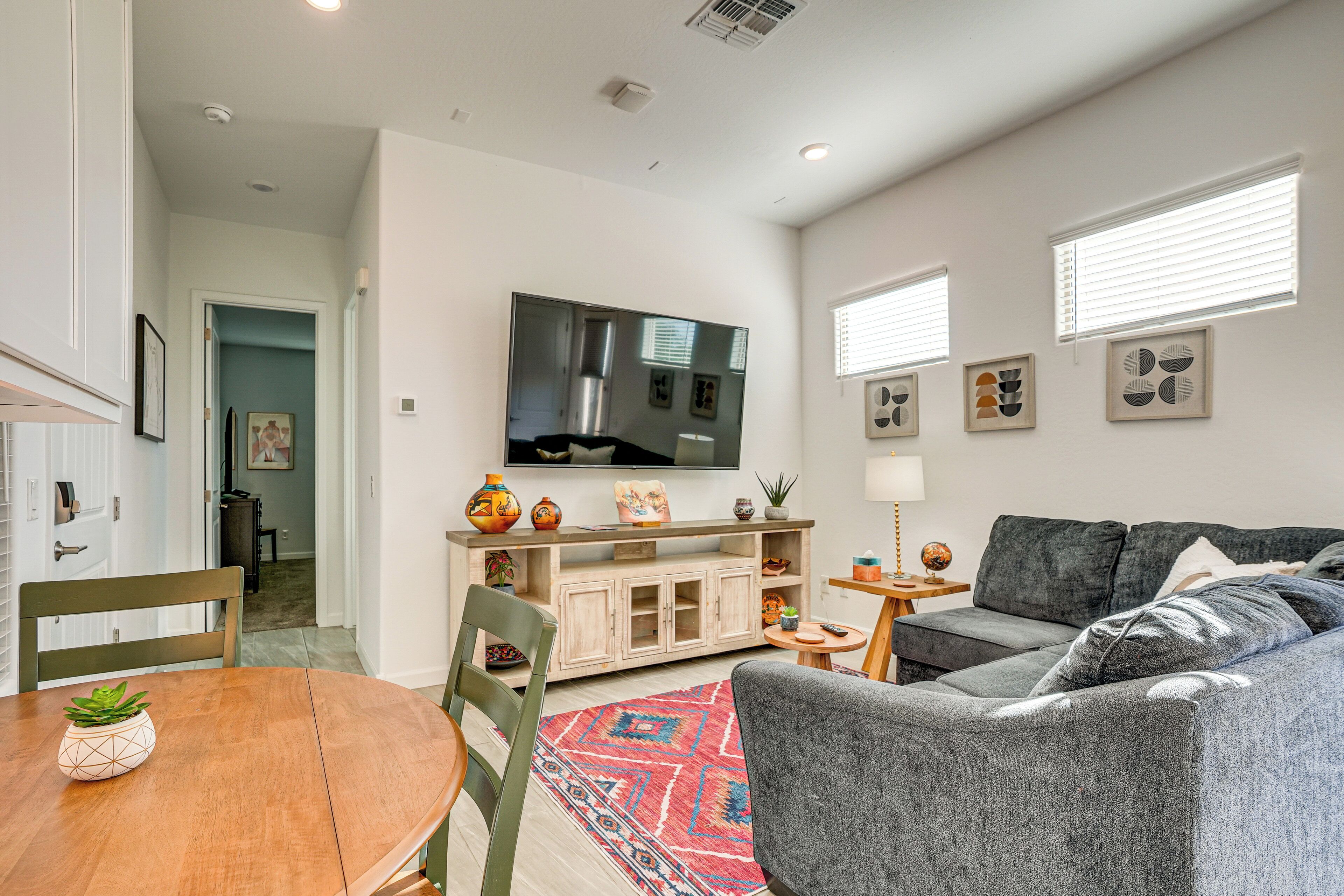 Una sala de estar moderna con un sofá gris, una mesa de comedor de madera y un televisor de pantalla plana montado en la pared.