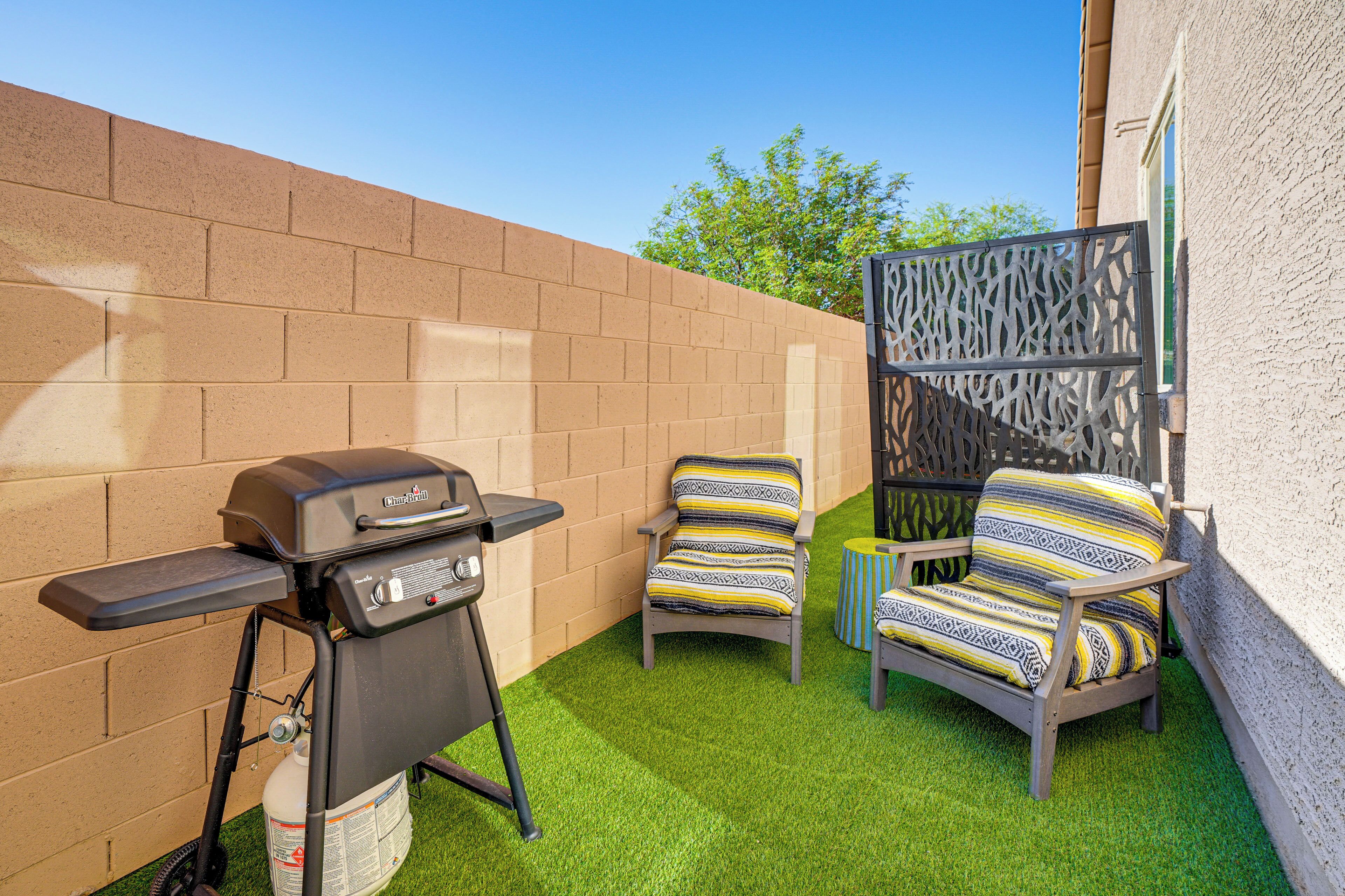 A backyard with a barbecue grill, two chairs with patterned cushions, and a decorative fence.