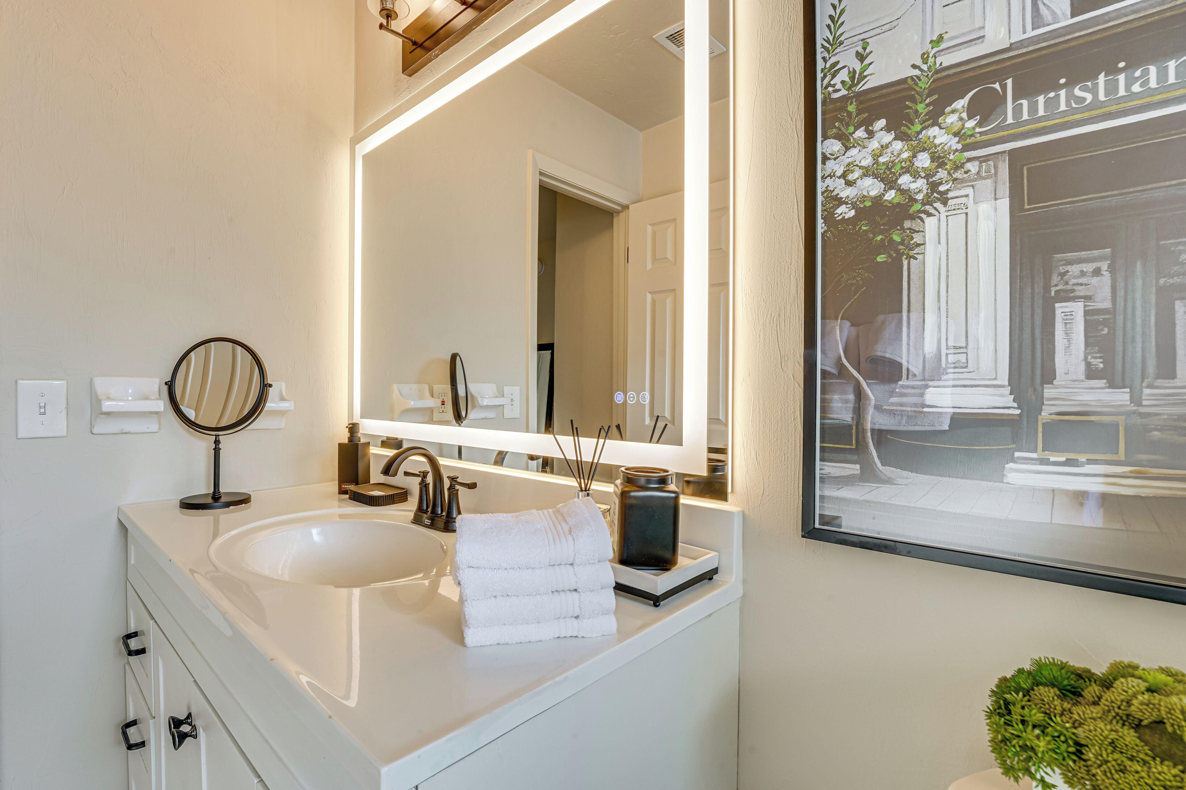 A bathroom with a large mirror, a sink, and a framed picture of a building.
