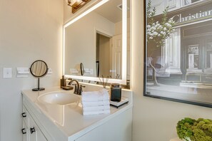 Un baño con un espejo grande, un lavamanos y un cuadro enmarcado de un edificio.