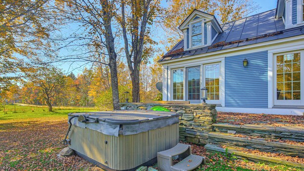 A hot tub in a yard with a stone wall and wooden steps, next to a house with large windows and a stone chimney. - Vermont Retreat w/ Hot Tub: Romantic Getaway (Rochester)