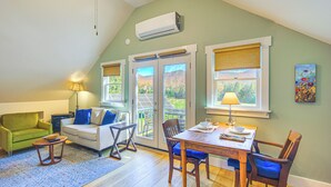 A cozy living room with a green couch, a wooden dining table, and a large window with a view of the outdoors. - Vermont Retreat w/ Hot Tub: Romantic Getaway (Rochester)