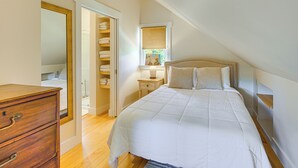 A bedroom with a bed, a wooden dresser, a walk-in closet, a bedside table with a lamp, and a window with a view of greenery. - Vermont Retreat w/ Hot Tub: Romantic Getaway (Rochester)