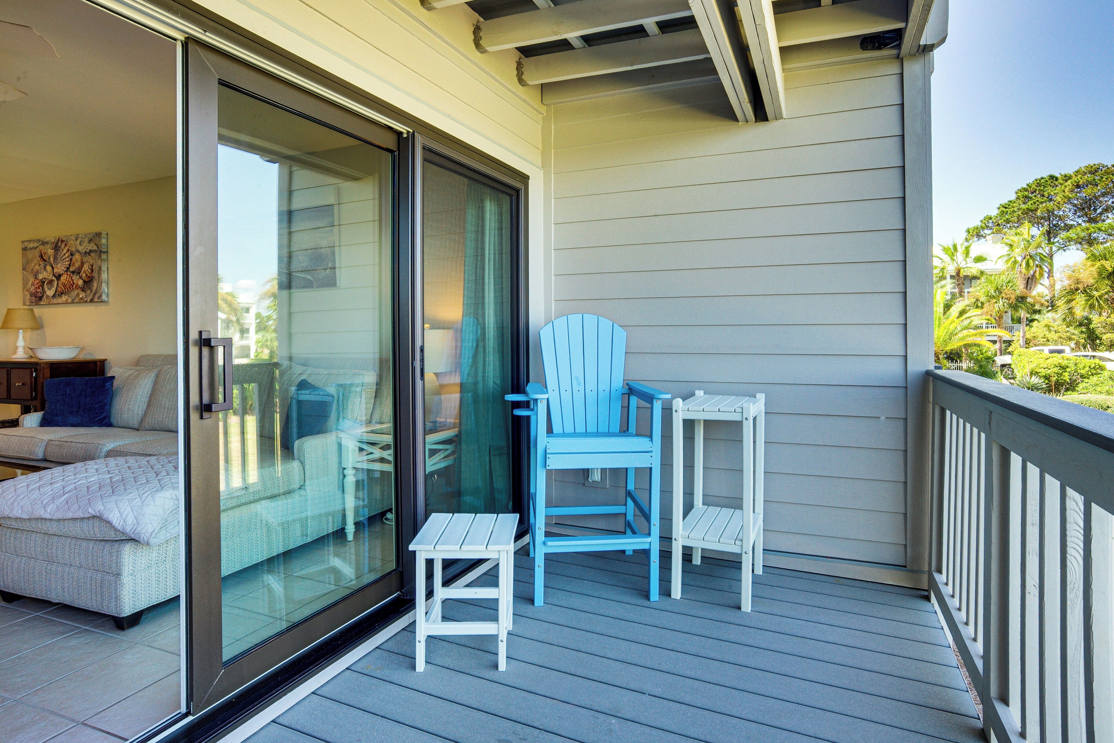 A balcony with a sliding glass door, a blue Adirondack chair, and a small white table.