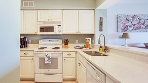 A kitchen with white cabinets, a microwave, stove, sink, and a decorative seashell painting. - Poolside Fun & Ocean Strolls: Harbor Island Haven! (Harbor Island)