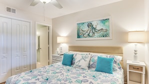 A bedroom with a bed, two nightstands, a ceiling fan, a door, and a painting on the wall. - Poolside Fun & Ocean Strolls: Harbor Island Haven! (Harbor Island)
