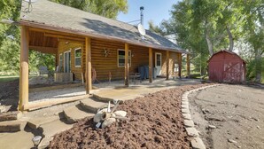 Une cabane en bois avec un porche couvert, une cheminée et, au fond, une grange rouge.