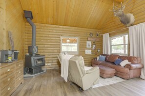 A log cabin interior with a fireplace, leather sofa, and a mounted deer head.