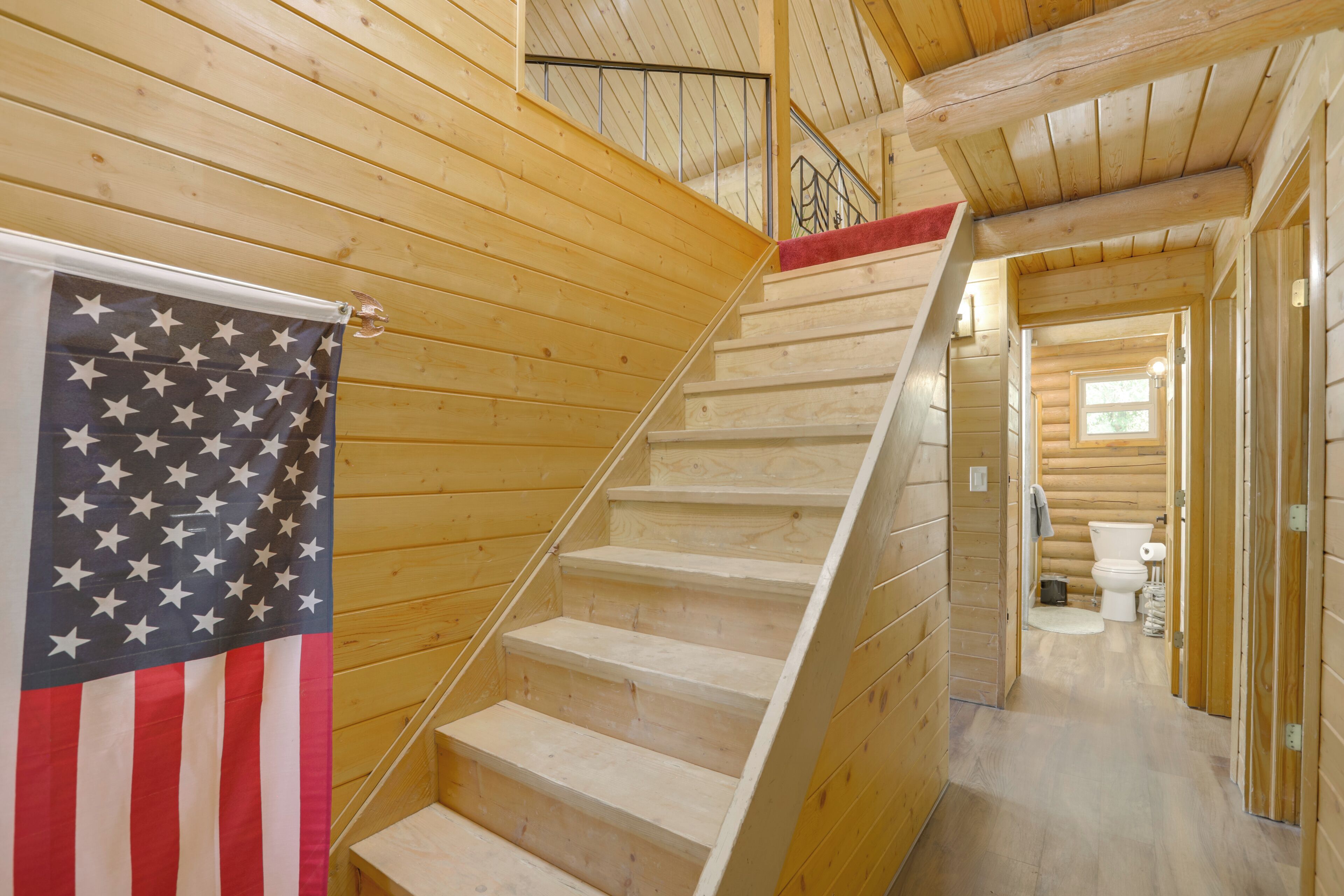 A wooden staircase with a flag, leading to a room with a toilet and a sink.