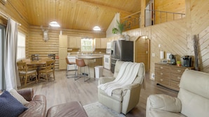 L’intérieur d’une cabane en rondins comprend un coin repas, une cuisine et un salon avec un canapé et un fauteuil inclinable.