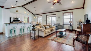 A spacious living area with a sofa, coffee table, and bar stools. There is a kitchen area with a microwave and cabinets. The room has large windows and a ceiling fan. - Private Beach & Views! Stilted Ocean Springs Home (Ocean Springs)