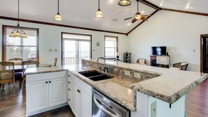 A spacious kitchen with granite countertops, a dishwasher, and a large island with a sink. There are hanging pendant lights and a ceiling fan. - Private Beach & Views! Stilted Ocean Springs Home (Ocean Springs)