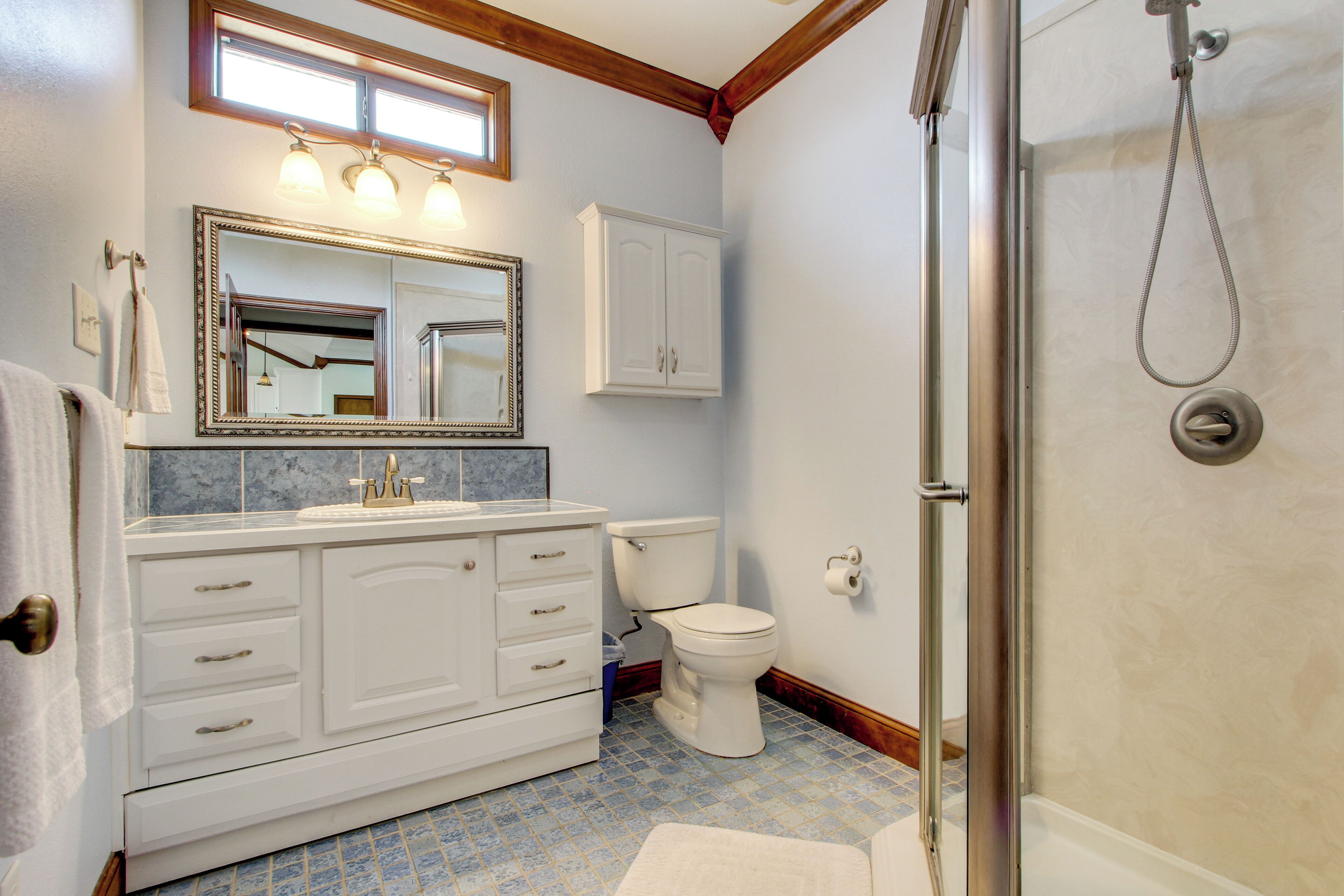 Een badkamer met een wit wastafelmeubel, een grote spiegel, een toilet en een douchehoek.