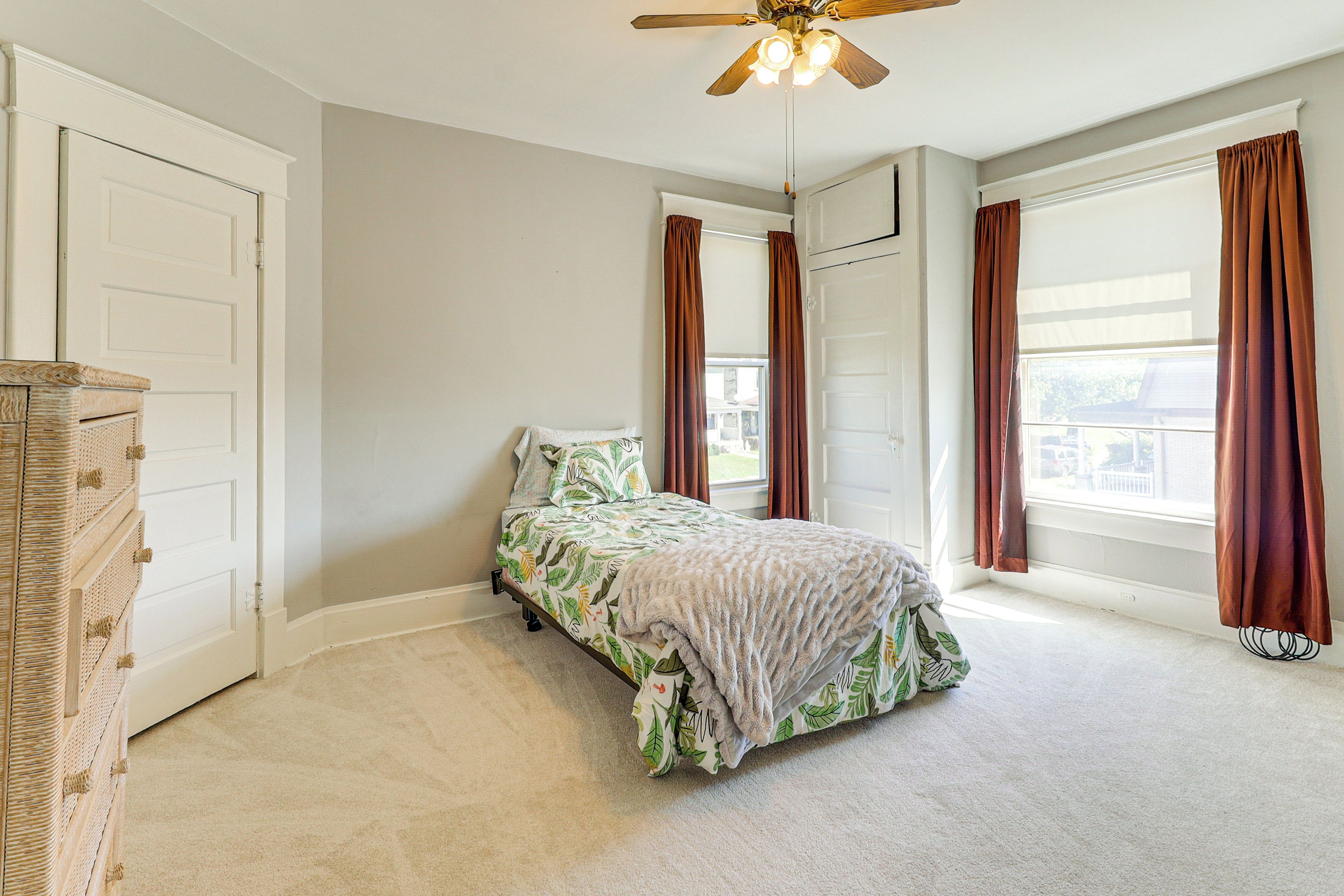 Un dormitorio con cama, ventilador de techo, ventana con cortinas y una puerta.