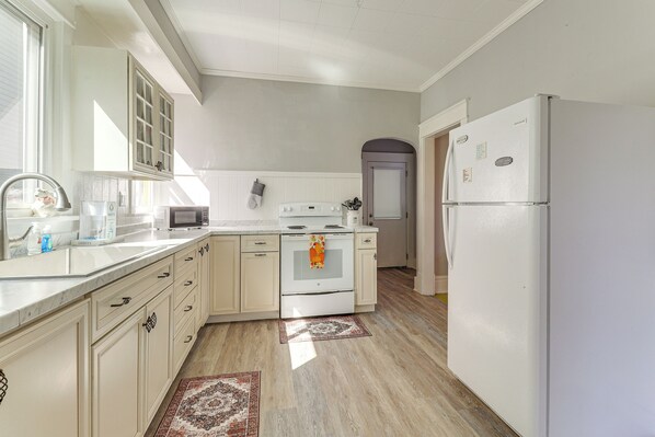 Una cocina con gabinetes blancos, estufa, refrigerador y microondas.