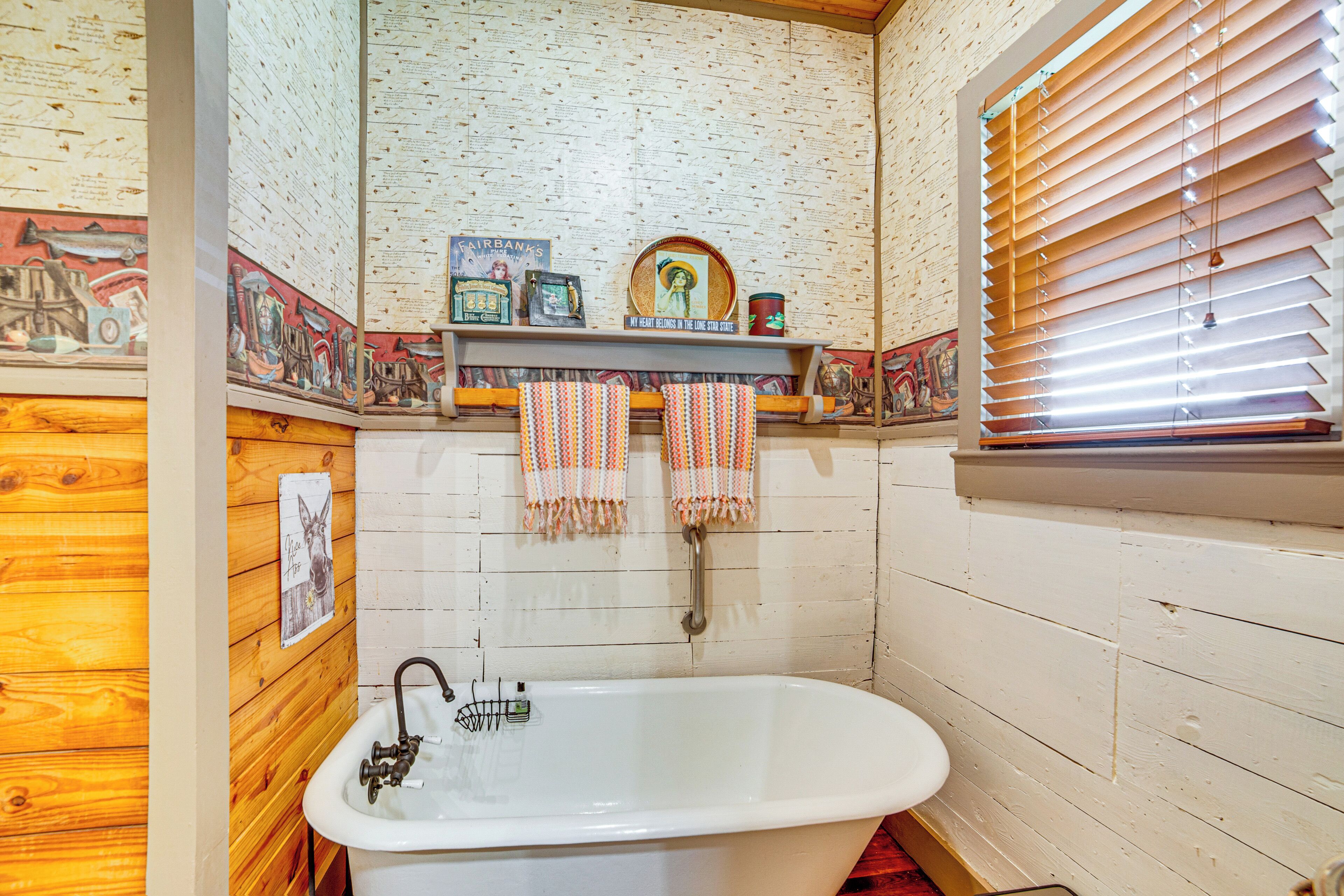 Un baño con pared de madera, una bañera blanca y un estante con toallas y objetos decorativos.