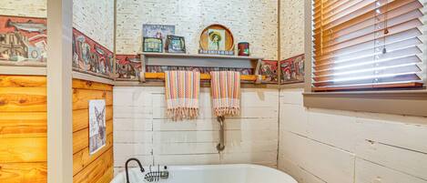 Un baño con pared de madera, una bañera blanca y un estante con toallas y objetos decorativos.
