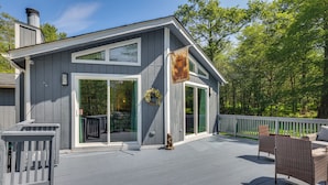 A gray house with a deck, a wreath, and a bear flag. - Yard + Game Room: Wooded Poconos Retreat (Tobyhanna)