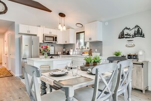Uma cozinha moderna com armários brancos, uma ilha central e uma área de jantar com mesa e cadeiras.