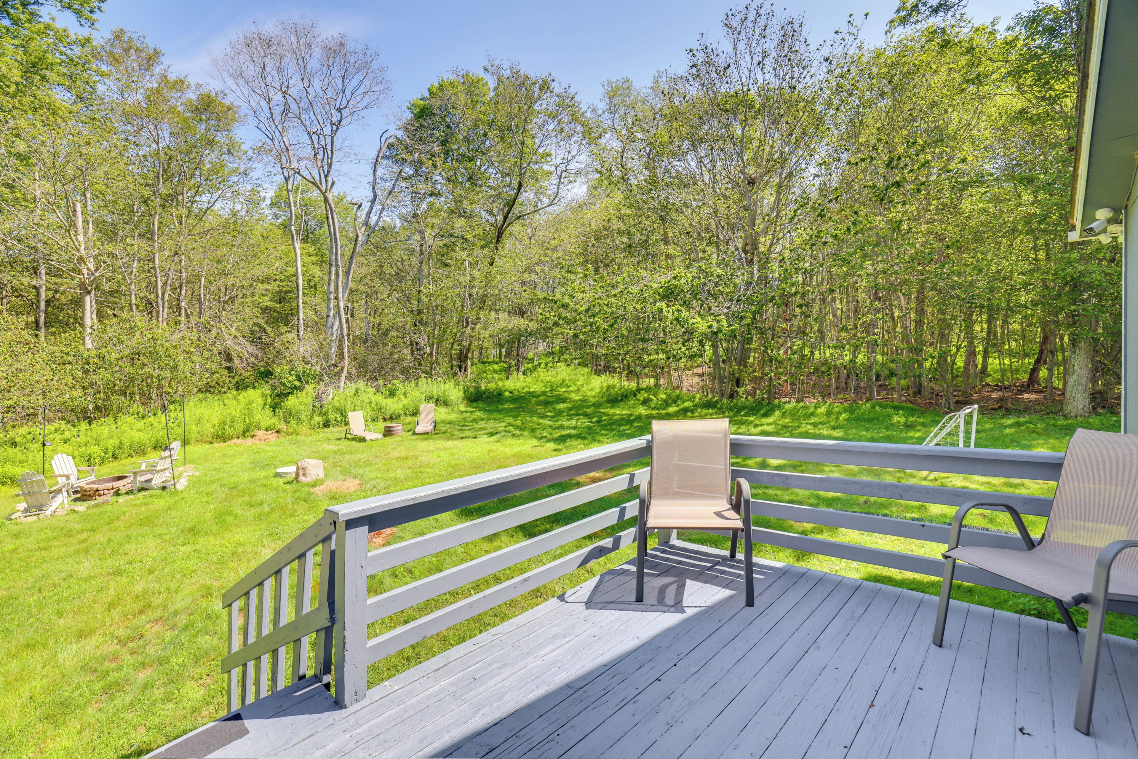 A wooden deck with a bench and a chair, overlooking a grassy area with trees.