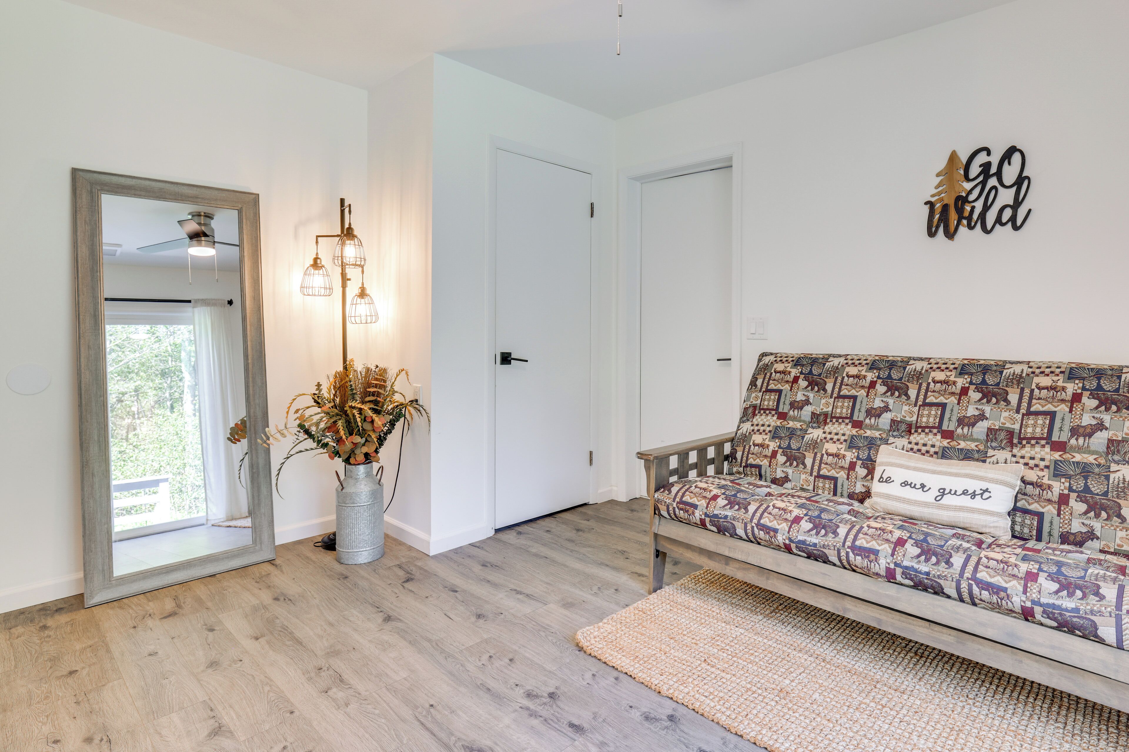 Une pièce avec un plancher en bois, un canapé agrémenté d’un coussin à motifs, un luminaire fixé au mur et une porte.
