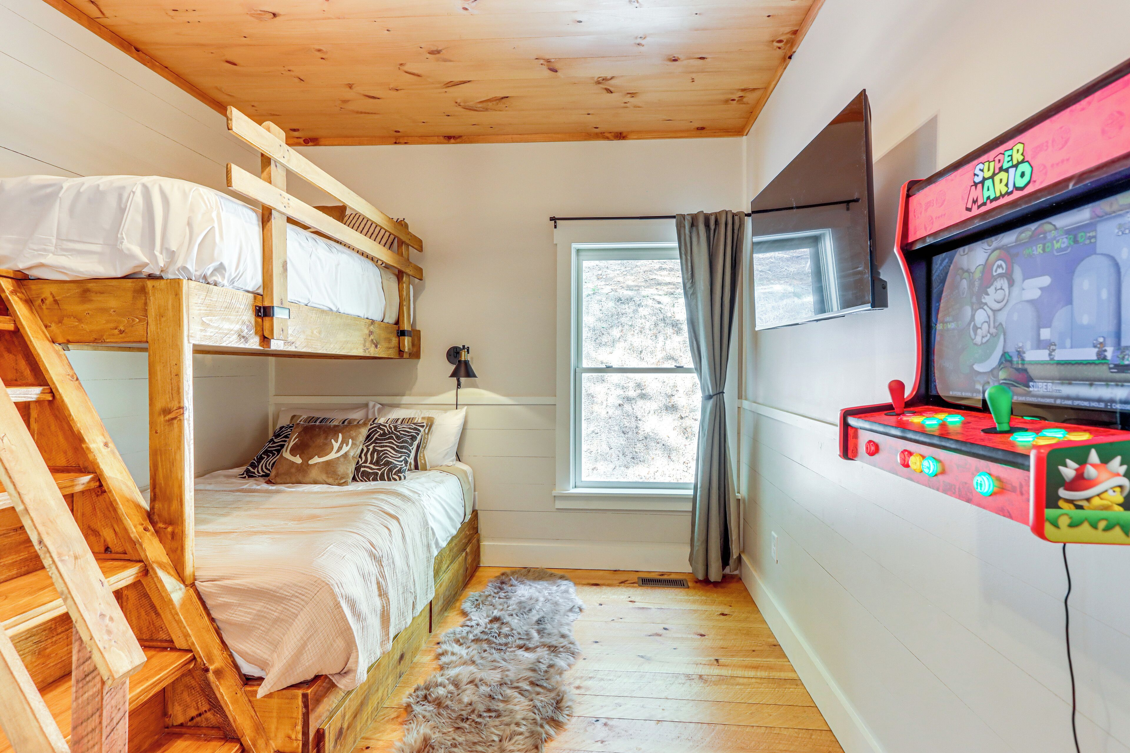 Een kamer met een stapelbed, een raam met gordijnen, een lamp en een Super Mario arcadekast.