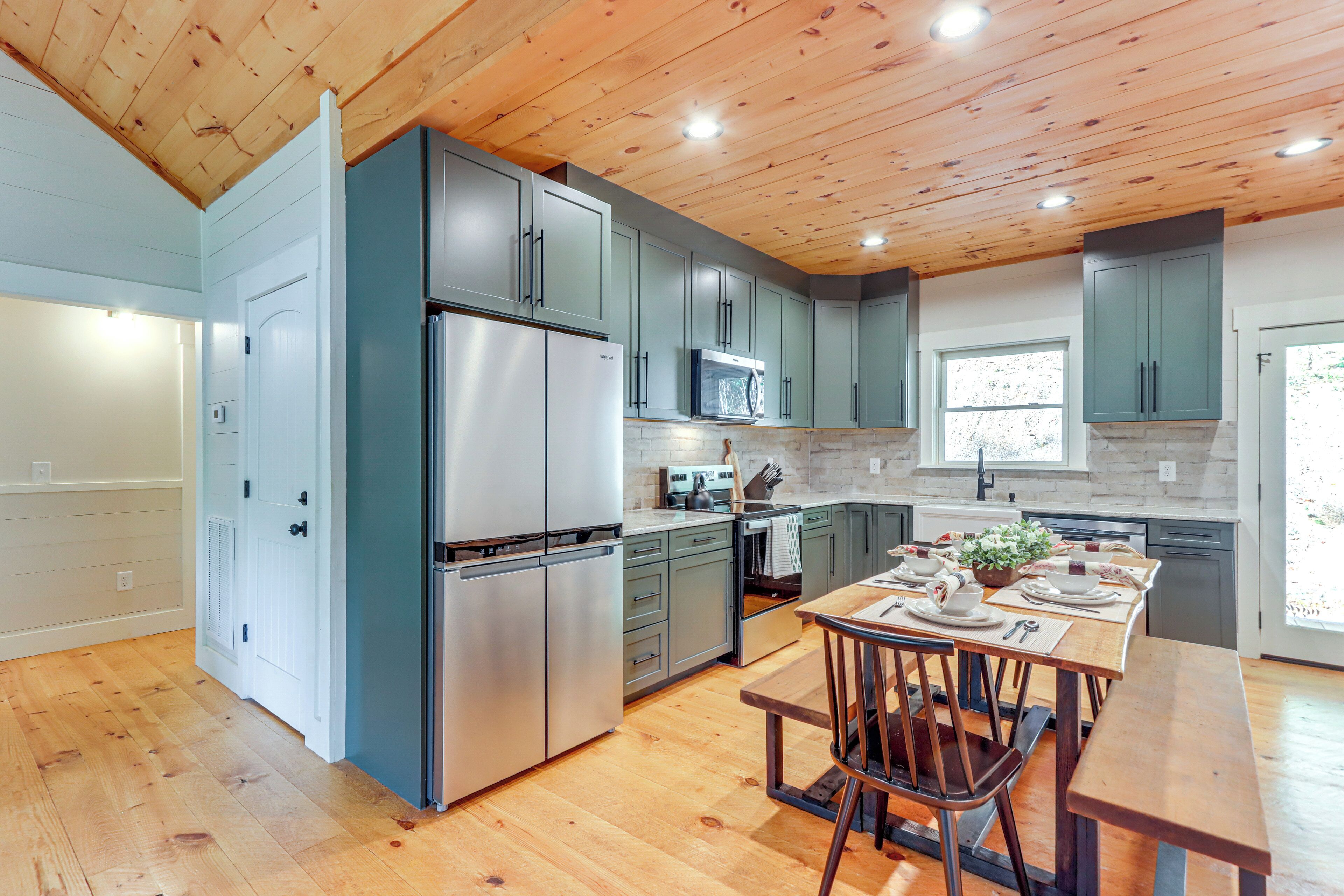 A modern kitchen with wooden ceiling, stainless steel appliances, and a dining area with a wooden table and chairs.